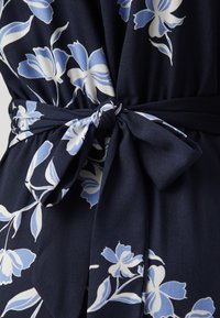 Abito in tessuto navy con grande motivo floreale blu e bianco, con dettaglio della cintura legata in vita e una texture morbida e liscia.