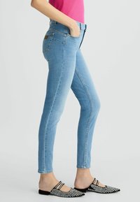 Šviesiai mėlynos džinsinės slim fit kelnės su aukštu liemeniu, turinčios penkias kišenes ir prekės ženklo odinį ženkliuką. Poruojamos su juodais smeigėmis dekoruotais mūlais.