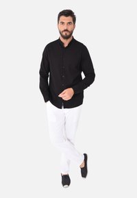 Camicetta nera a maniche lunghe con colletto alla mandarina, con chiusura a bottoni, abbinata a pantaloni bianchi in lino e espadrillas scure. Design semplice e aderente.