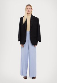 Overmaat zwarte blazer, beige aansluitend topje, lichtblauwe wijduitlopende broek en zwarte sandalen. Gelaagd stof met gestructureerde silhouette.