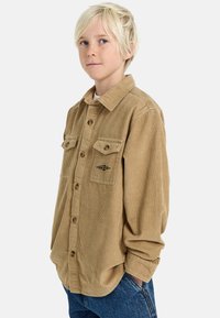Camicia button-up in corduroy marrone con due tasche frontali e dettaglio del logo, maniche lunghe, vestibilità rilassata e tessuto a coste testurizzato.