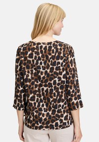 Leopardenmuster-Bluse mit lockerer Passform, Dreiviertelärmeln und Rundhalsausschnitt. Farben sind Braun, Schwarz und Creme. Strukturierter Stoff.