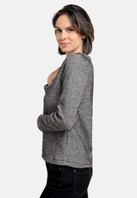 Grauer Herringbone-Strickpullover mit langen Ärmeln, weitem Rundhalsausschnitt und lockerer Passform, getragen mit schwarzen Hosen vor einem neutralen Hintergrund.