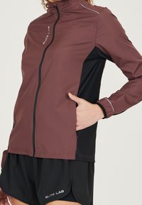 Bordowo-czarna kurtka z wysokim kołnierzem, zamkiem błyskawicznym i odblaskowymi elementami. Wykonana z lekkiego materiału, posiada boczne kieszenie.