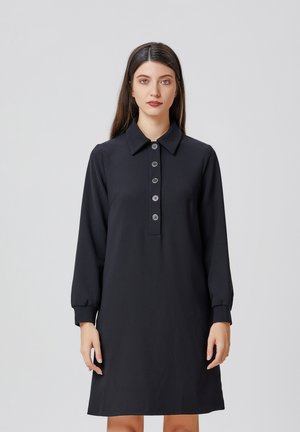 Robe noire à col, avec des manches longues et une patte de boutonnage. Fabriquée en tissu lisse, elle est dotée de cinq boutons ronds et de poignets fuselés.