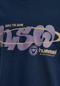 Marineblaue Sportbekleidungsstoff mit fettem Text "SERVE THE GAME" und dem "hummel SPORTSWEAR" Logo, das eine Biene in einem Kreis zeigt.