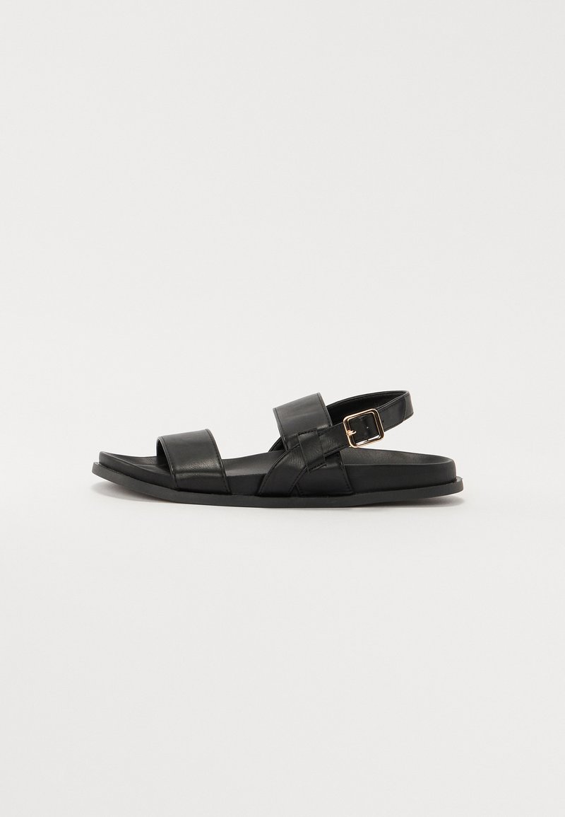 Sandalias de cuero negro con dos correas anchas, detalle de hebilla y suela plana. Textura suave con un diseño minimalista y punta abierta.