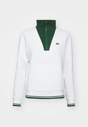 Weißer Pullover mit grünem Stehkragen und Reißverschluss, ausgestattet mit einer Kängurutasche und gestreiften grünen Akzenten an den Bündchen und dem Saum. Lacoste-Logo angebracht.