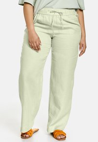 Pantalon en lin vert claire à coupe décontractée, taille élastique avec cordon de serrage ; assorti à des sandales orange à brides.