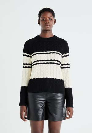 Pull à mailles noir et crème avec un motif à rayures horizontales, doté d'un col rond et de bords côtelés aux manches et à l'ourlet. Short en cuir en dessous.