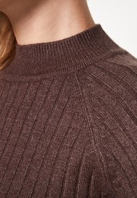 Bruine geribde trui met een hoge hals en een gestructureerde stof, die verticale lijnen en een zachte uitstraling toont.