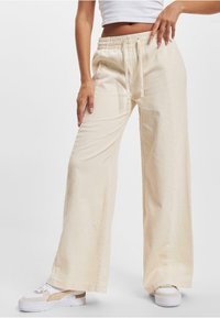Beige Corduroyhosen im weiten Schnitt mit elastischem Bund, Kordelzug und seitlichem Stickdetail, kombiniert mit weißen Plateausneakern.