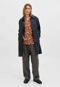 Abrigo negro sobre una camisa floral roja, pantalones de pierna ancha grises y zapatos negros. La tela parece suave con un ajuste relajado y botones en la parte delantera.