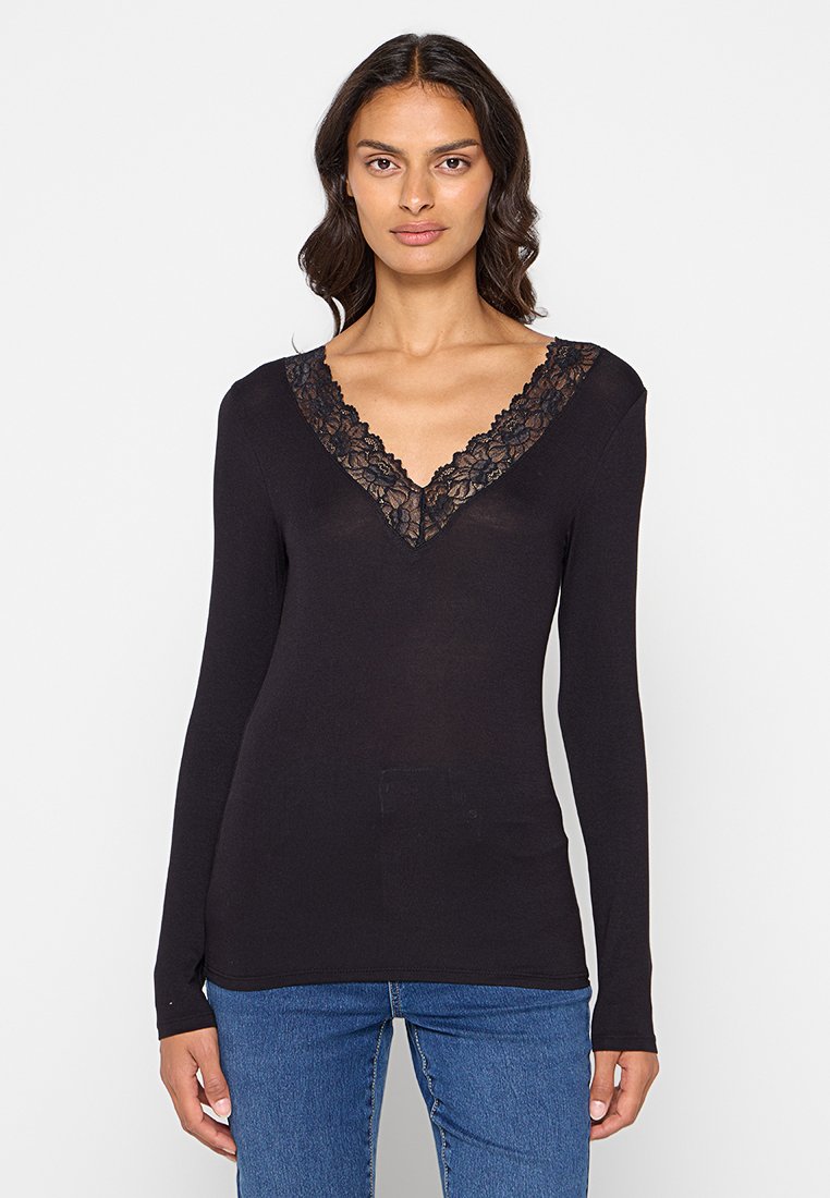 Top nero a maniche lunghe con scollatura a V decorata da un bordo in pizzo nero. Il tessuto è liscio e aderente, abbinato a jeans blu.