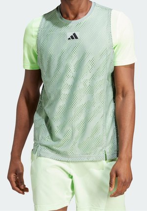 Camiseta deportiva verde claro con diseño de malla, con cuello redondo, tirantes y un logo centrado en el pecho.