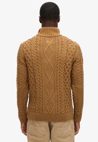 Brauner Strickpullover mit hohem Kragen und strukturiertem Zopfmuster. Verfügt über gerippte Bündchen und Saum sowie ein Rautenmuster auf der Rückseite.