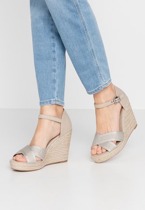 Sandalias de cuña beige con detalle trenzado de yute, con tiras cruzadas en plata con el nombre de la marca y correa en el tobillo para mayor soporte.