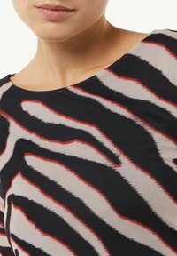 Schwarz-beige Oberteil mit einem auffälligen Zebra-Streifen-Muster in roten Akzenten; glatte Textur mit Rundhalsausschnitt und kurzen Ärmeln.