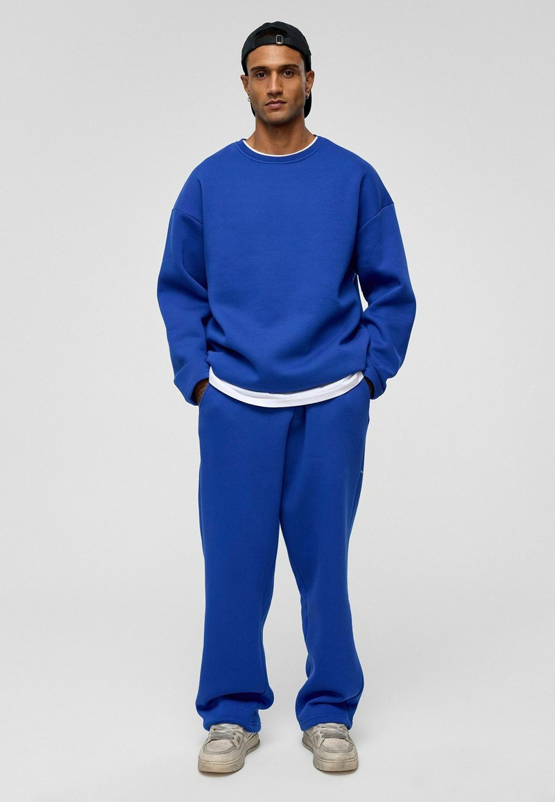 Blauwe sweatshirt en bijpassende sweatpants in een relaxte pasvorm, gemaakt van zacht materiaal. Heeft wijde mouwen, ribgebreide manchetten en een gelaagde look met een witte shirt eronder.
