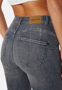 Grå denimjeans med mid-rise passform, med en brun läderlapp på midjebandet och två bakfickor med sömdetaljer.