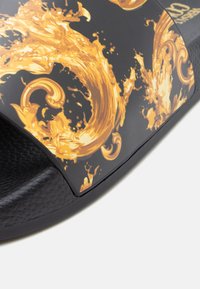 Sandália slide preta com design texturizado e padrões dourados em espiral e salpicos numa superfície mate. Palmilha texturizada para aderência.