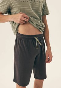 Jasnozielona koszulka w paski z krótkimi rękawami, włożona do spodenek w ciemnoszarym kolorze, z elastycznym paskiem i sznurkiem.