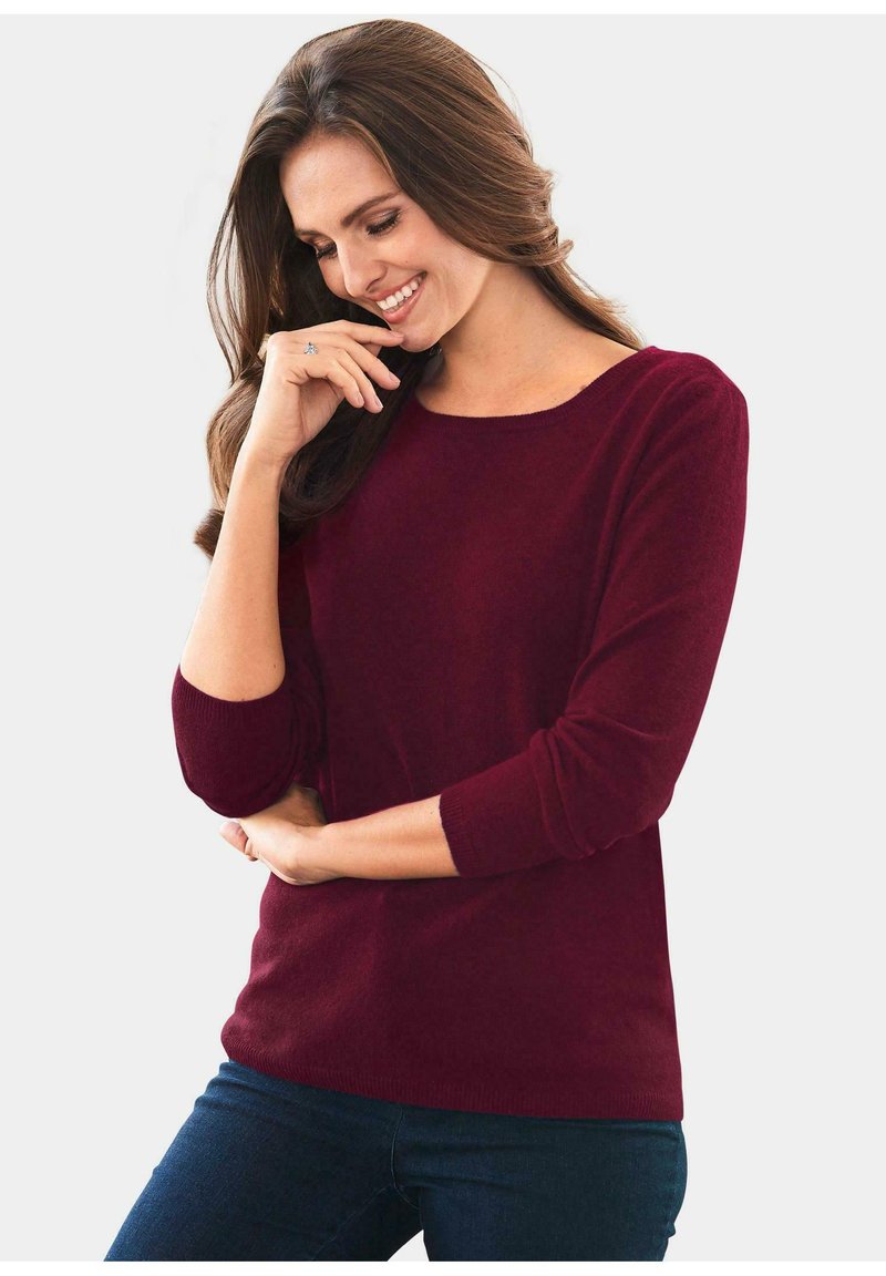 Burgunderfarbener, langärmeliger Strickpullover mit Rundhalsausschnitt und gerippten Bündchen. Weiche Textur und taillierte Passform, kombiniert mit dunkelblauen Jeans.