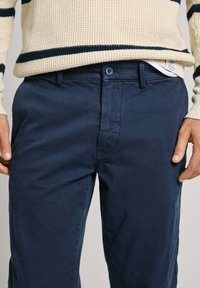 Marina blå chinos i bomull med rak passform, framfickor och knäppning, samt en mjuk textur.