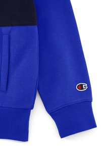 Felpa blu con parte superiore nera, tessuto testurizzato, logo ricamato sulla manica, polsini elasticizzati e apertura della tasca laterale.