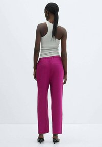 Fuchsia trousers with a straight-leg design and elastic waistband, paired with a light grey tank top. Model viewed from the back.