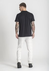 Camiseta negra de manga corta, combinada con pantalones de chándal claros con un diseño geométrico. Zapatillas negras con superficie texturizada.