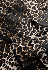 Tissu à imprimé léopard avec des boutons noirs et une ceinture assortie dotée d'une boucle rectangulaire en écaille, sur un vêtement.