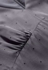 Tessuto grigio con piccoli pois neri, dal texture arricciata. Materiale liscio e leggero con una leggera lucentezza.