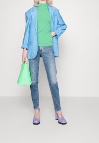 Blazer de rayas azul claro, Suéter de cuello alto verde, Jeans azul claro, Zapatos de tacón lavanda y un bolso acolchado verde lima.
