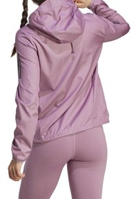 Leichter, lavendelfarbener Windbreaker mit Kapuze, elastischen Bündchen und Saum. Verfügt über eine subtile Textur und schwarze Streifen entlang der Ärmel.