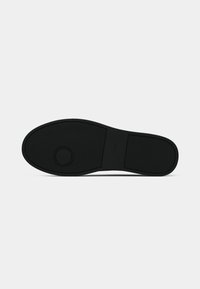 Suola di scarpa in gomma nera con superficie texturizzata e dettaglio a motivo circolare. Design piatto, segni minimi e senza colori o accenti aggiuntivi.