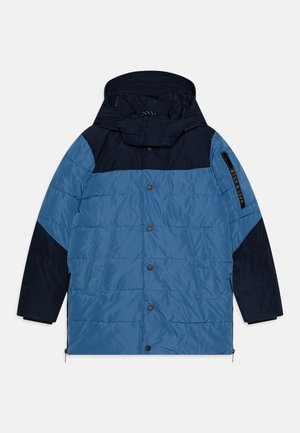 Polstret jakke i blå og marineblå. Har høy krage, trykknapper og sidelommer. Glatt tekstur og sporty design.