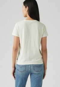 Camiseta de manga corta color beige claro con escote redondo, de textura suave y un ajuste ligeramente holgado, combinada con jeans de mezclilla azul.