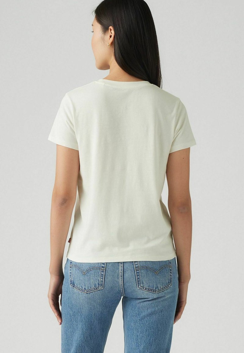 T-shirt beige clair à manches courtes avec un col rond, texture douce et coupe légèrement décontractée, associé à un jean en denim bleu.