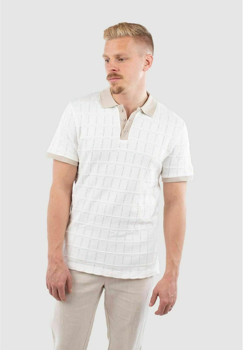 Polo shirt blanc à manches courtes avec un motif texturé, col plat en tissé beige, patte de boutonnage à deux boutons, associé à un pantalon de couleur claire.