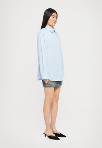 Camicia azzurra chiara con colletto, maniche lunghe sagomate e vestibilità comoda, abbinata a una gonna di jeans e mule nere con tacco.