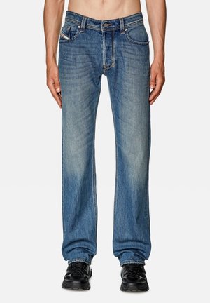 Jeans de mezclilla azul con un diseño de pierna recta, lavado desgastado, cinco bolsillos y botón en la bragueta. El usuario los combina con zapatillas negras.