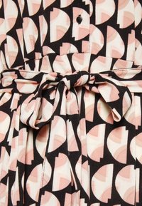 Schwarz-rosa-creamfarbener Stoff mit geometrischem Muster, der zu einer Schleife gebunden ist, mit einem sichtbaren schwarzen Knopf über dem Knoten.
