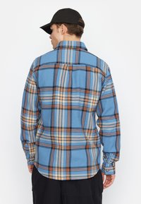 Blauw en oranje geruite shirt met een knoopsluiting, lange mouwen en een gladde textuur, met een gebogen zoom en kraag.