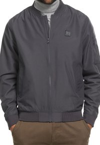 Grijze bomberjack met een gesloten rits aan de voorkant, ribbelmanchetten en -zoom, en subtiele logodetails op de borst. Glad, lichtgewicht stof.