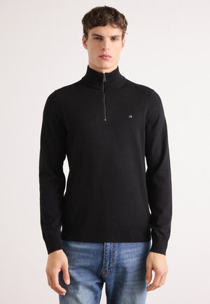 Black zip-up sweater with a high collar, long sleeves, and logo detail. Made from a smooth fabric, features a fitted design and ribbed cuffs.
