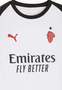 Maglia sportiva bianca con accenti neri, presenta un colletto nero. Include il logo Puma rosso e un emblema di fiamma rossa, con il testo nero "Emirates FLY BETTER".
