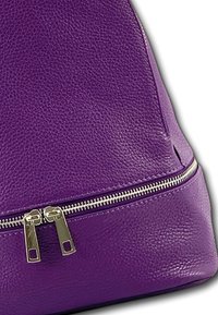 Sac en cuir violet avec une surface texturée, équipé d'une fermeture éclair en argent et de tirettes en bas. Design arrondi avec des accents minimaux.