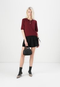 Pulover polo cu mânecă scurtă în culoarea burgundă, cu două butoane, fustă plisată neagră, șosete închise la culoare și geantă de mână neagră, cu o textură bine definită.