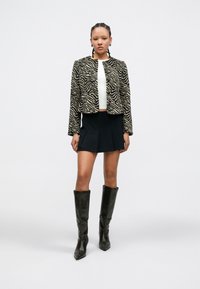 Chaqueta recortada con estampado de cebra, falda negra y botas de cuero marrón hasta la rodilla. Textura suave, diseño estructurado y colores contrastantes.